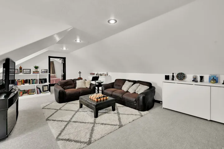Carpeted attic space featuring white sloped ceilings and recessed lighting