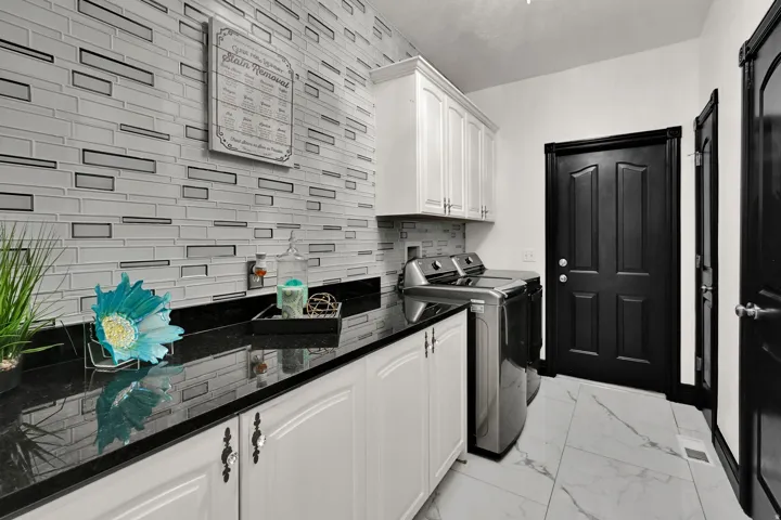 Functional utility area featuring a mosaic tile backsplash, black countertops, white cabinetry, and large format floor tiling