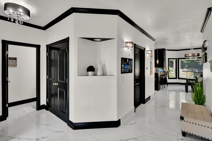 Hallway featuring white marble-look tile flooring, contrasting black trim and doors, recessed lighting in a built-in niche, and decorative wall sconces