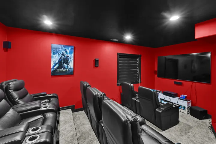 Dedicated media room featuring tiered seating, recessed lighting, and rich red walls with a contrasting black ceiling