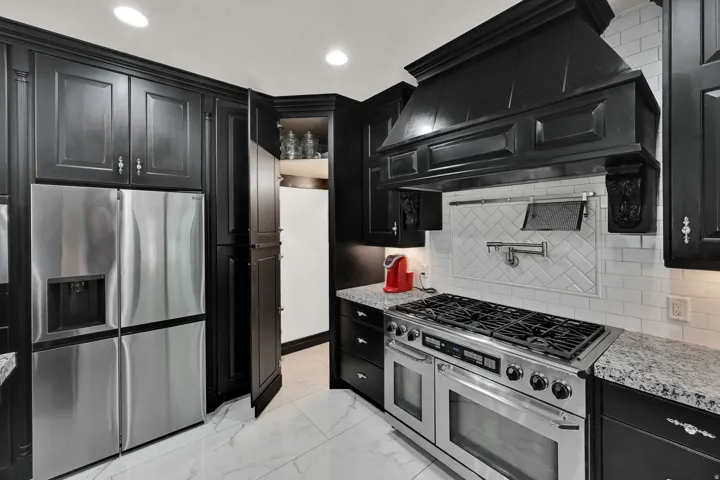 Gourmet kitchen featuring a professional-grade range, custom black cabinetry, stainless steel appliances, granite countertops, and a white subway tile backsplash