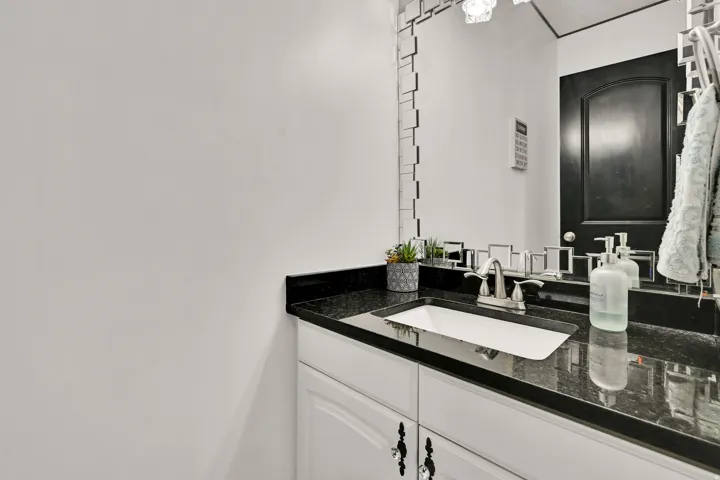 Bathroom vanity featuring a black granite countertop with an undermount sink, brushed nickel faucet, and white cabinetry