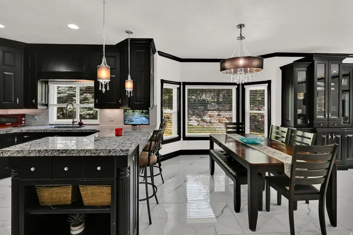 Modern kitchen and dining area featuring black cabinetry, granite countertops, and white tile flooring