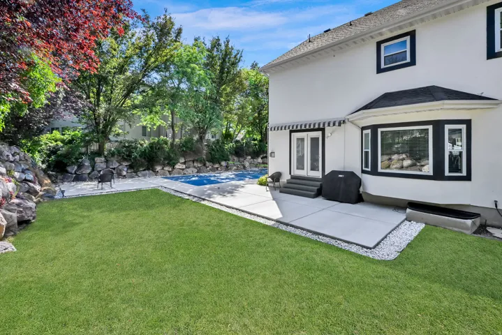 Expansive green lawn bordering a concrete patio with a covered pool