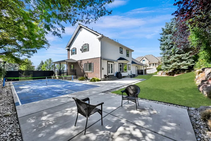 Expansive backyard featuring a multi-sport court with blue surfacing, a concrete patio, and a manicured lawn