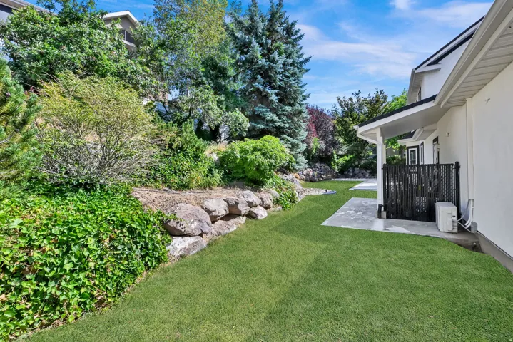 Spacious rear yard featuring an expansive lawn, concrete patio areas, and a rock retaining wall