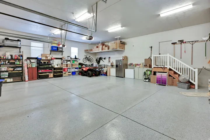 Spacious garage with epoxy-coated concrete flooring, overhead fluorescent lighting, and built-in shelving units