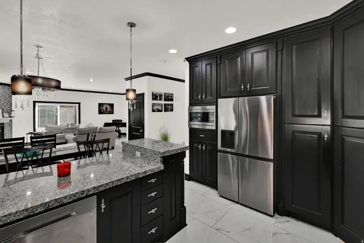 Kitchen island with light granite countertops, black cabinetry, and built-in dishwasher