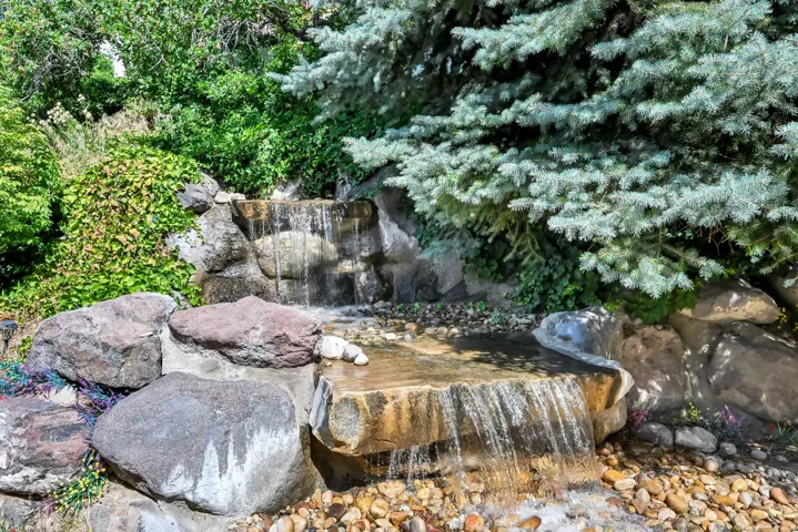Tiered rock waterfall feature surrounded by lush greenery and mature evergreen trees