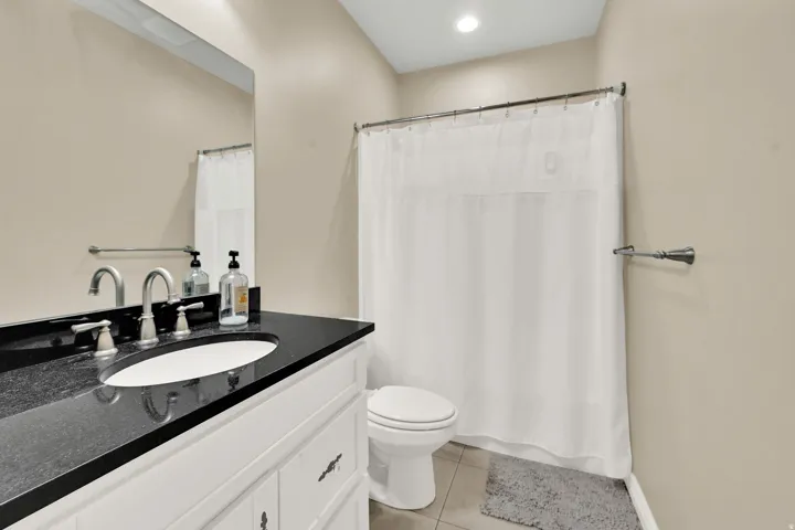Bathroom featuring a white vanity with paneling and dark hardware, black countertop, and an oval undermount sink with brushed nickel fixtures