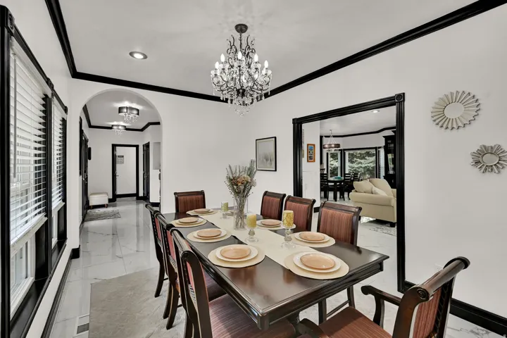 Formal dining area featuring a dark wood table and chairs, a central chandelier, recessed lighting, and white walls with contrasting dark trim