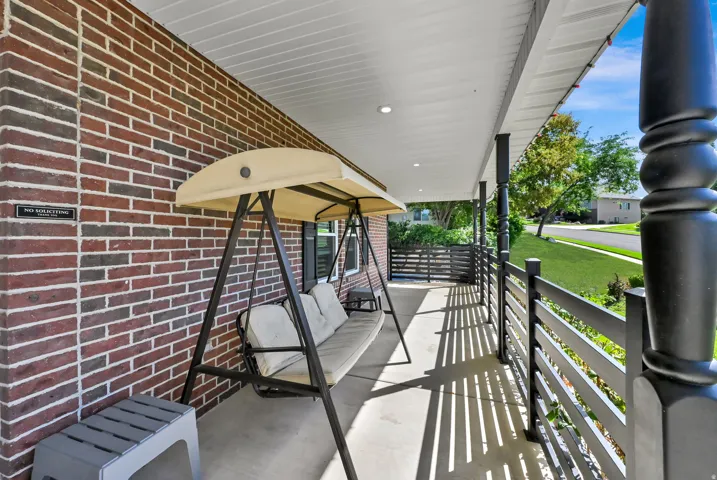 Covered porch featuring a brick exterior wall, white soffit ceiling with recessed lighting, and a dark-toned railing system