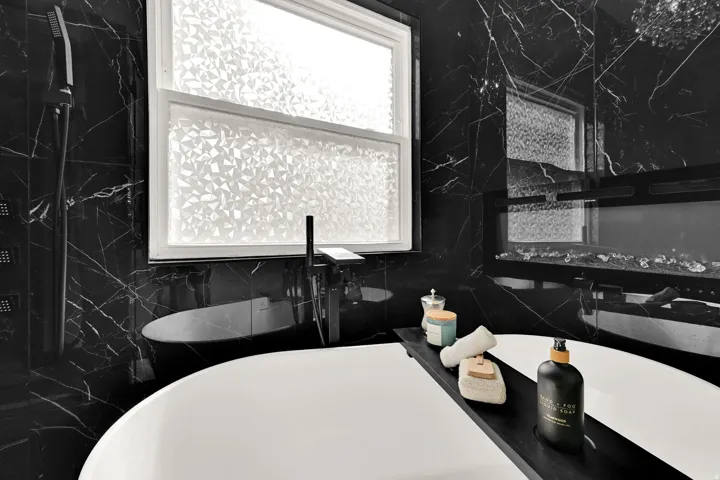 Freestanding soaking tub featuring a matte black floor-mounted faucet and black marble wall tile