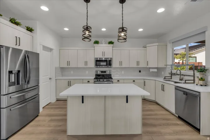 Modern kitchen featuring a central island with a solid surface countertop, stainless steel appliances, light wood-finish cabinetry, a subway tile backsplash, and recessed lighting