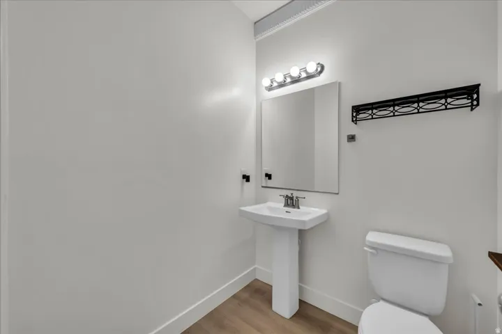 Pedestal sink featuring a chrome faucet, illuminated by a four-bulb vanity light, with wood-finish flooring