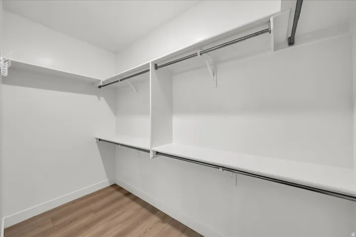 Walk-in closet featuring wood-finish flooring, white walls, and built-in shelving with hanging rods