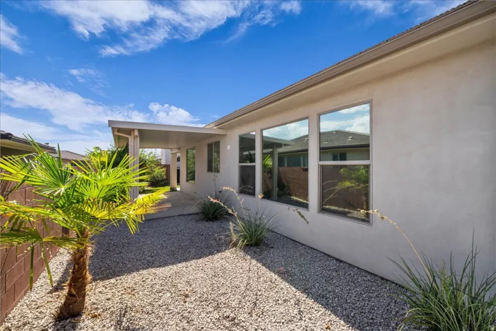 Stucco exterior with multiple windows, covered patio area, and drought-tolerant landscaping with gravel and a palm tree