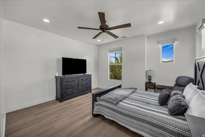 Bedroom featuring wood-finish flooring, recessed lighting, a ceiling fan, and two windows with roller shades