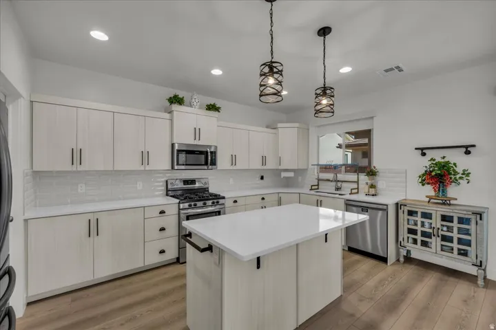 Kitchen featuring light wood-finish cabinetry, white countertops, stainless steel appliances, and wood-finish flooring