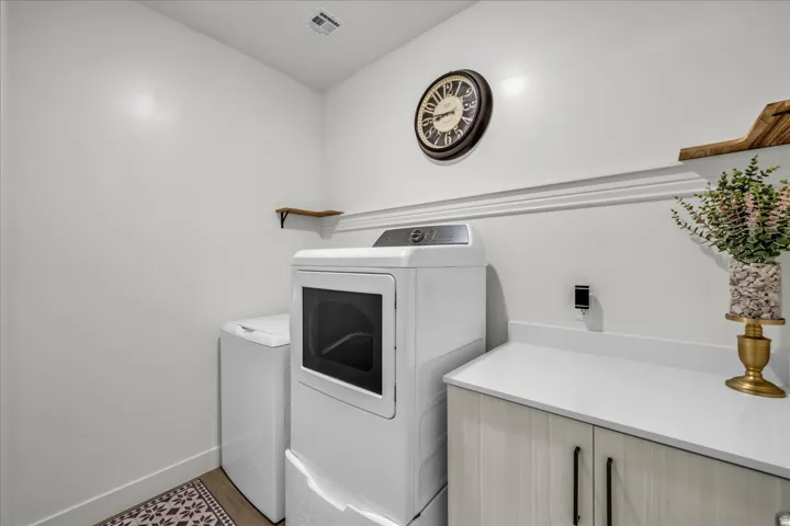 Dedicated laundry area featuring a built-in countertop, light wood-finish cabinetry with black hardware, and white wall trim