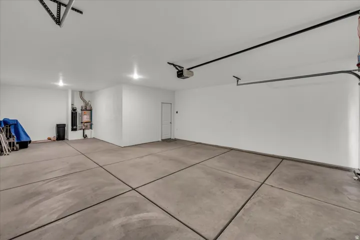 Spacious garage featuring a concrete floor, bright overhead lighting, a built-in water heater system, an overhead garage door opener, and a side access door