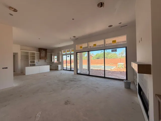Spacious open-concept living area featuring polished concrete flooring, abundant natural light from multi-panel sliding glass doors, recessed ceiling lighting, and a modern kitchen with white cabinetry and stainless steel appliances