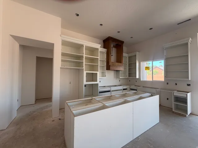 White cabinetry, a large central island, a wood-finish range hood, and a window with natural light