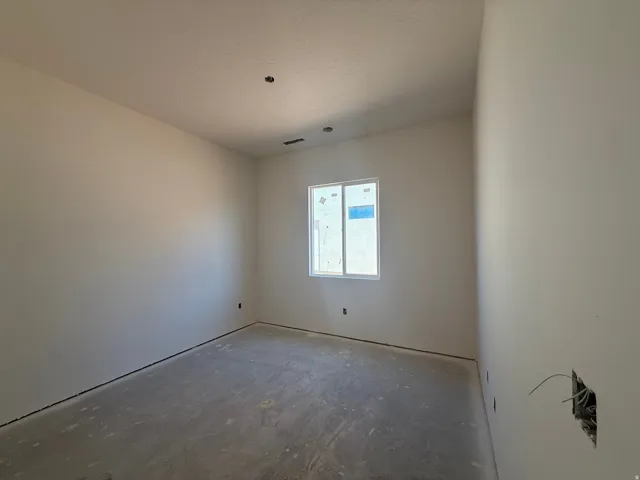 Bright, open room with abundant natural light from a large window, concrete flooring, and fresh drywall finish