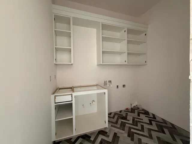 White cabinetry with open shelving, base cabinet with drawer, and chevron-patterned floor tile