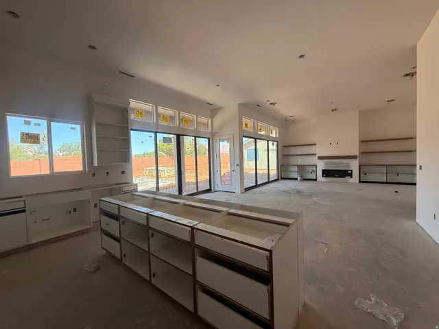 Spacious kitchen featuring a large center island with multiple drawer storage, stainless steel appliances, white cabinetry with upper glass-front shelving, quartz countertops, and expansive sliding glass doors that flood the space with natural light and a