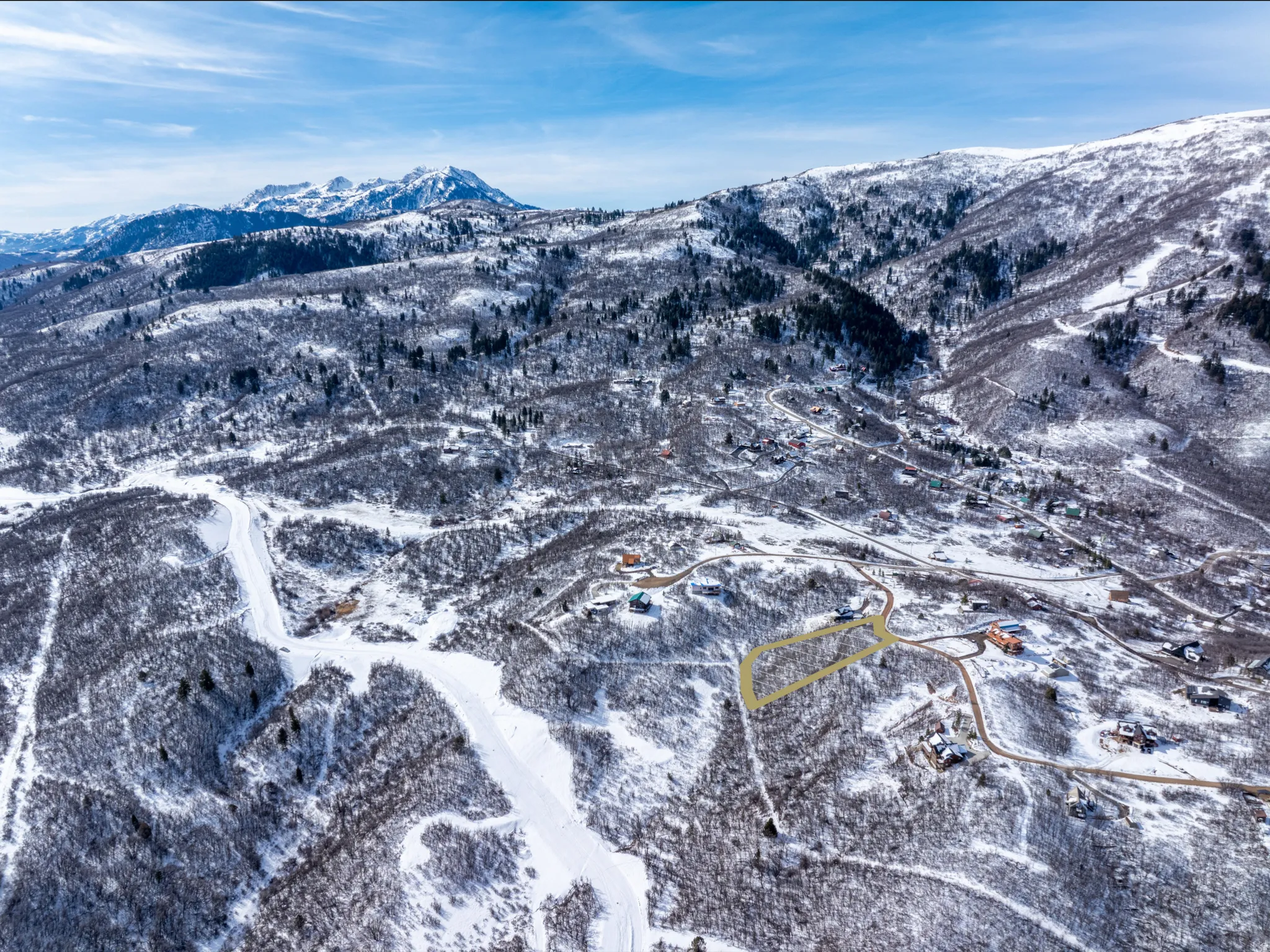 Expansive snow-covered mountain landscape featuring distant peaks, numerous residential properties, and winding roads