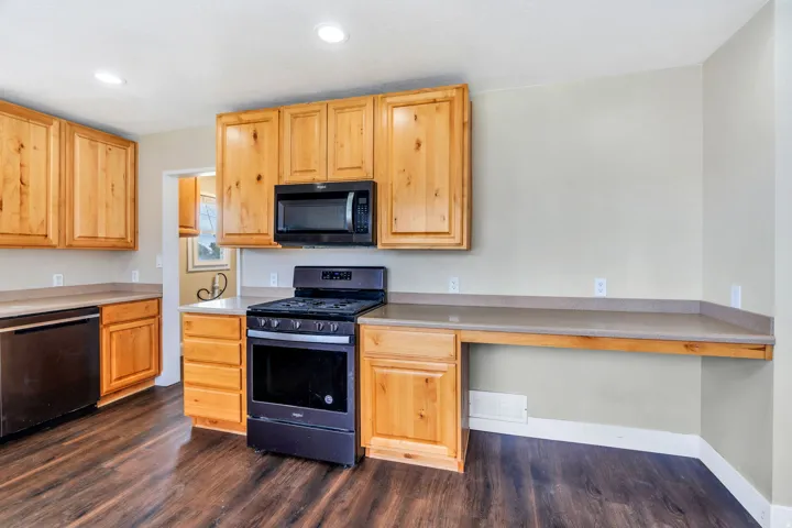 Kitchen featuring natural wood cabinetry, dark wood-finish flooring, recessed lighting, integrated black appliances, and light-toned countertops
