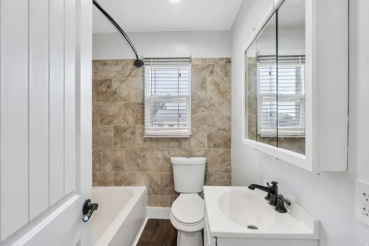 Bathroom featuring a white vanity with integrated sink, black hardware, an illuminated medicine cabinet, and a bathtub with tiled surround