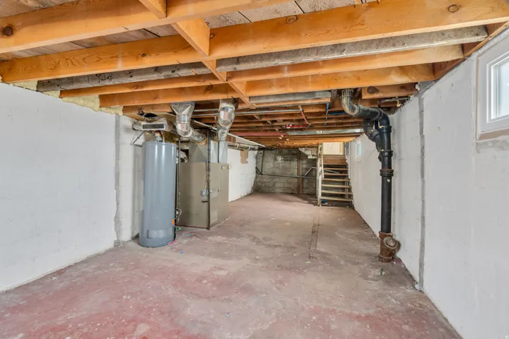 Expansive unfinished basement featuring exposed ceiling joists, white-painted block walls, and a concrete floor