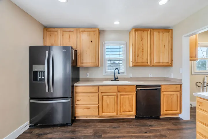 Kitchen featuring light wood cabinetry, light countertops, wood-finish flooring, a black French door refrigerator, and a black dishwasher