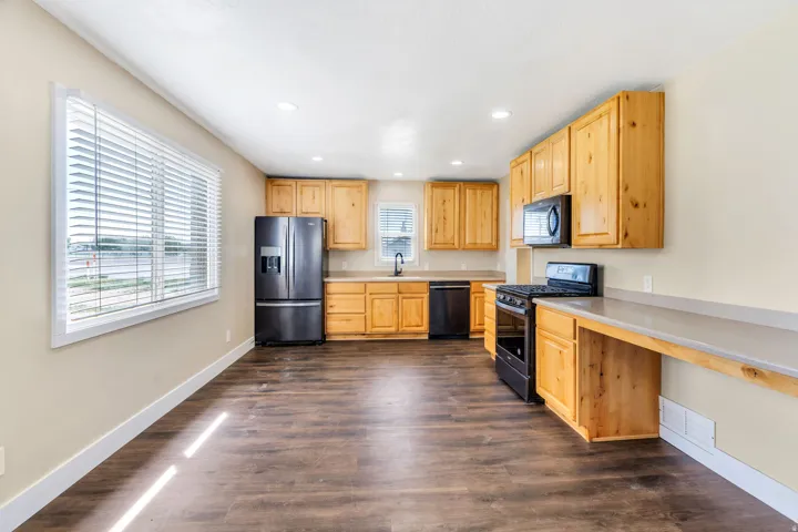 Kitchen featuring wood cabinetry, stainless steel-finish appliances, wood-finish flooring, and light-toned countertops