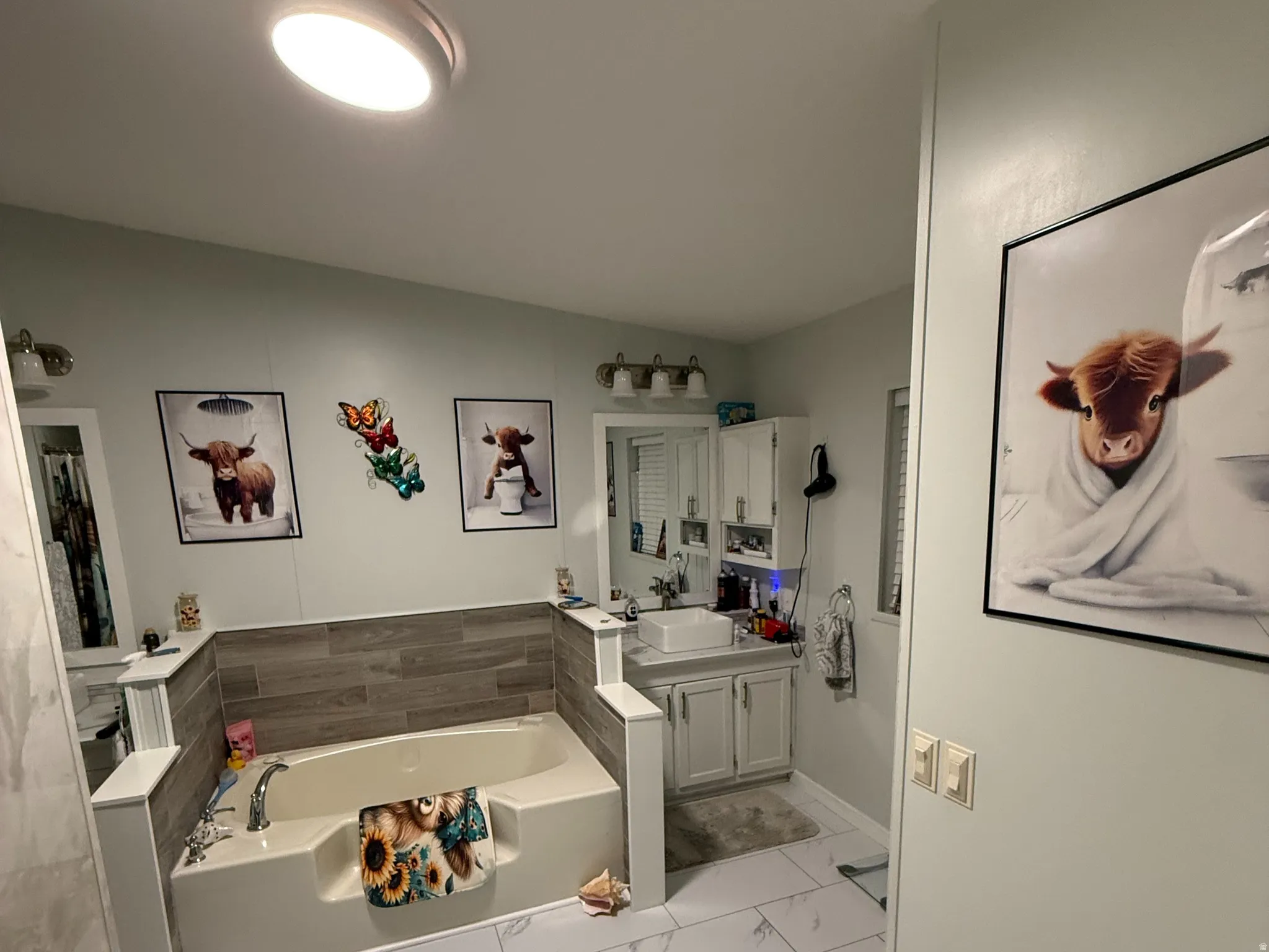 Bathroom featuring a built-in soaking tub, wood-finish accent wall, and a single vanity with a coordinating cabinet