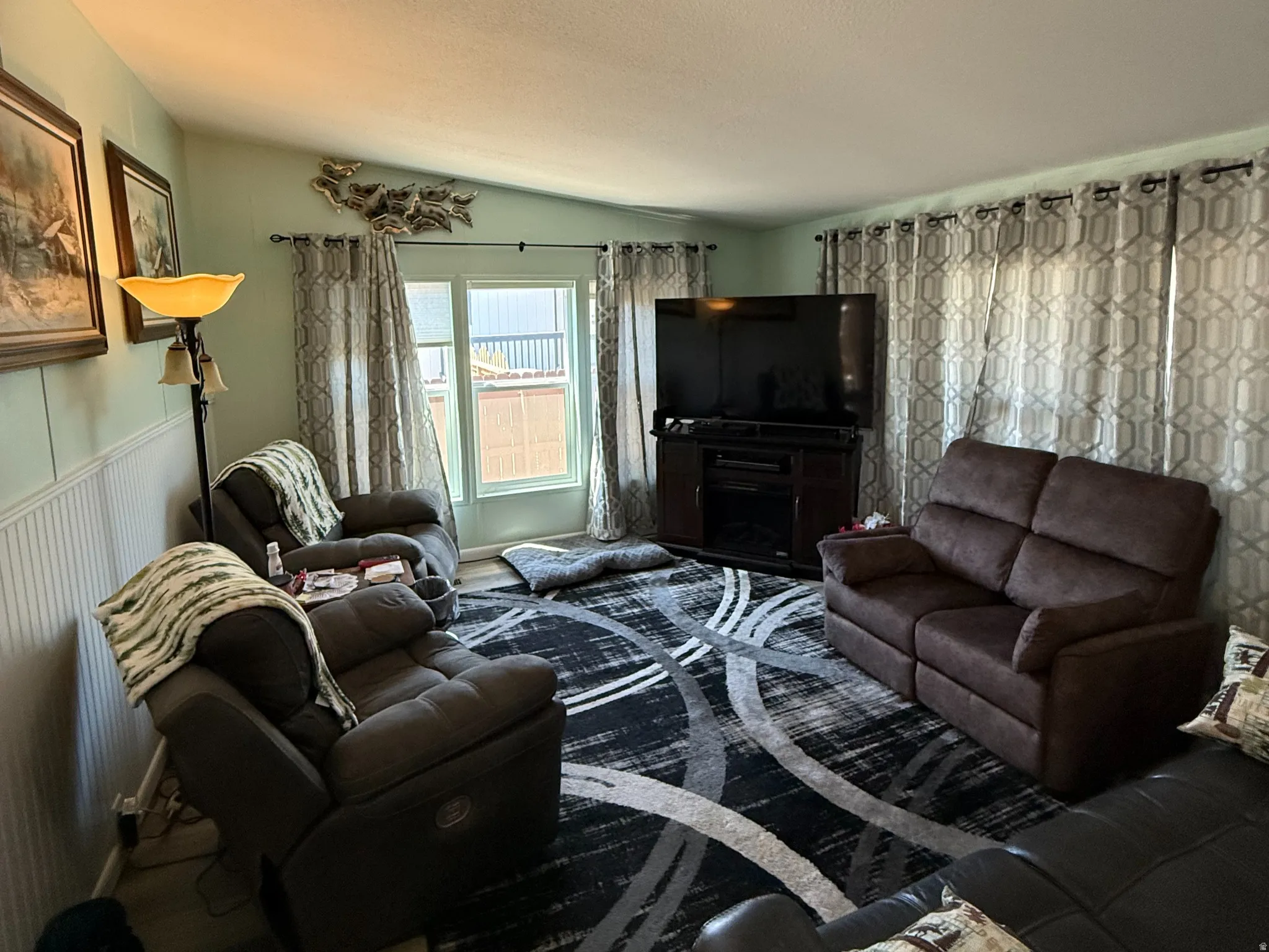 Living area featuring wood-finish flooring, white beadboard wainscoting, and a window with vertical blinds