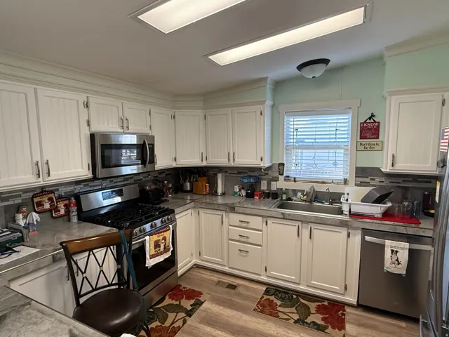 Kitchen featuring white paneled cabinetry, stainless steel appliances, grey countertop, mosaic tile backsplash, and wood-finish flooring