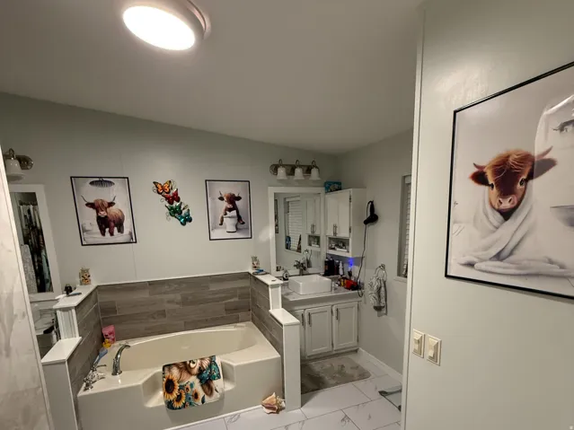 Bathroom featuring a built-in soaking tub, wood-finish accent wall, and a single vanity with a coordinating cabinet