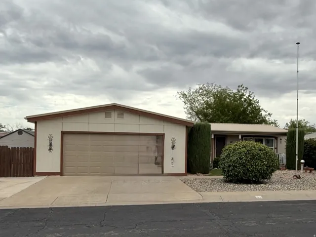 Exterior featuring a two-car garage with a panel door, a concrete driveway, and low-maintenance landscaping with decorative rock and mature shrubs