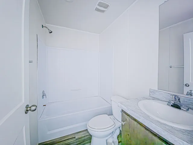 Bathroom featuring a combination shower and bathtub, a single vanity with an integrated sink, a wall-mounted mirror, and wood-finish flooring