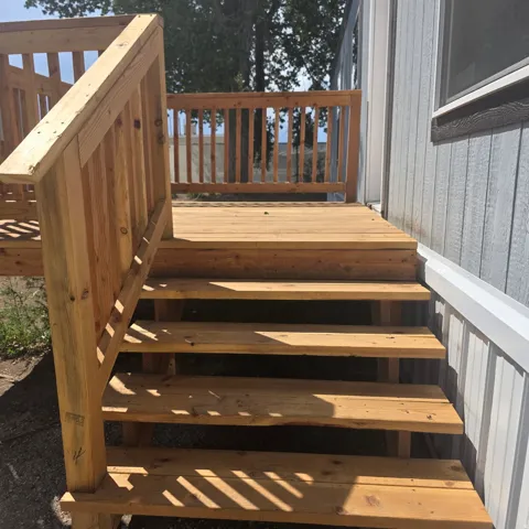 Exterior wooden deck with railing, featuring natural wood steps and light gray siding