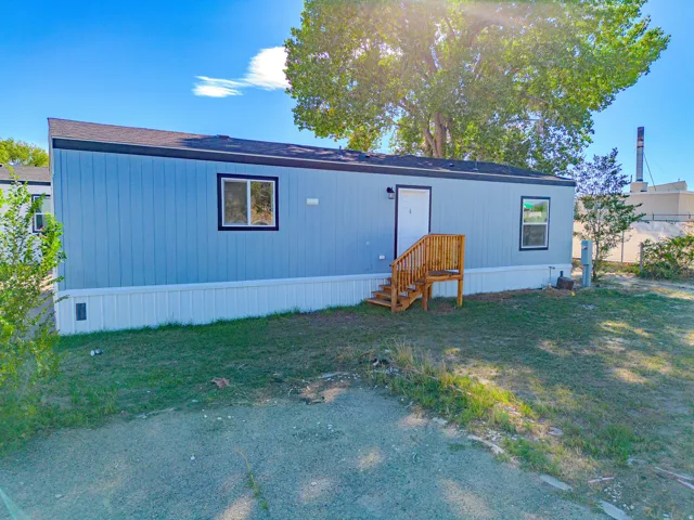 Blue vertical siding, white skirting, dark-framed windows, wood-finish steps, and a dark roof