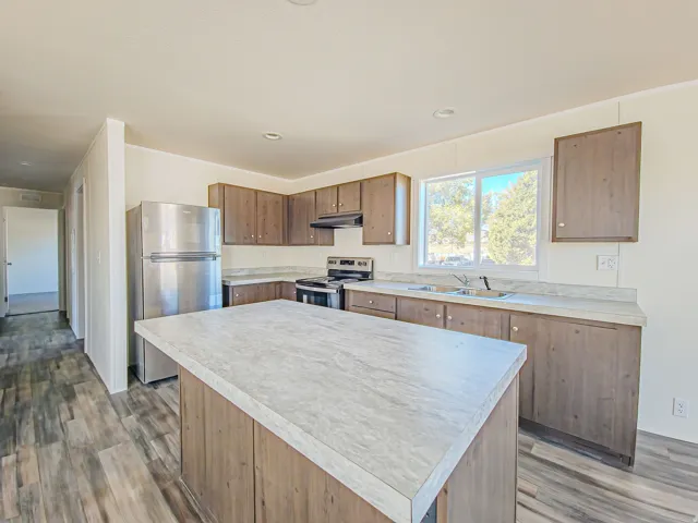 Kitchen featuring wood-finish cabinetry, stainless steel appliances, a center island with a light-toned countertop, and wood-finish flooring