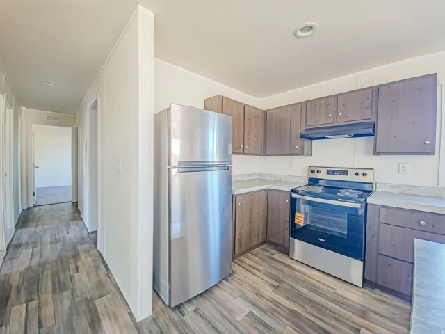 Kitchen featuring wood-finish flooring, stainless steel appliances, dark wood-finish cabinetry, and light-toned countertops