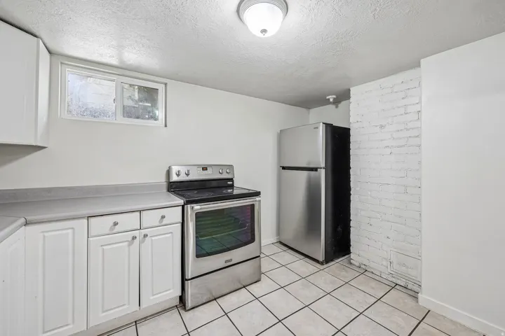 Kitchen featuring white cabinetry, a stainless steel range, a stainless steel refrigerator, white tiled flooring, and a white painted brick accent wall