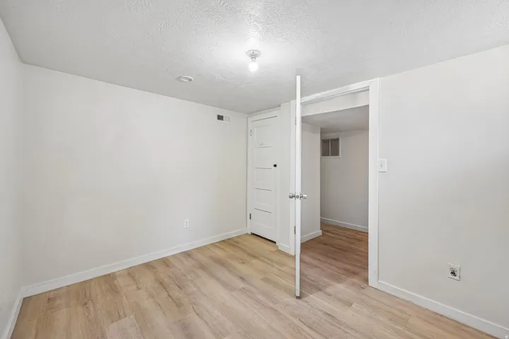 Bright, open bedroom with wood-finish flooring, white painted walls, and recessed ceiling lighting