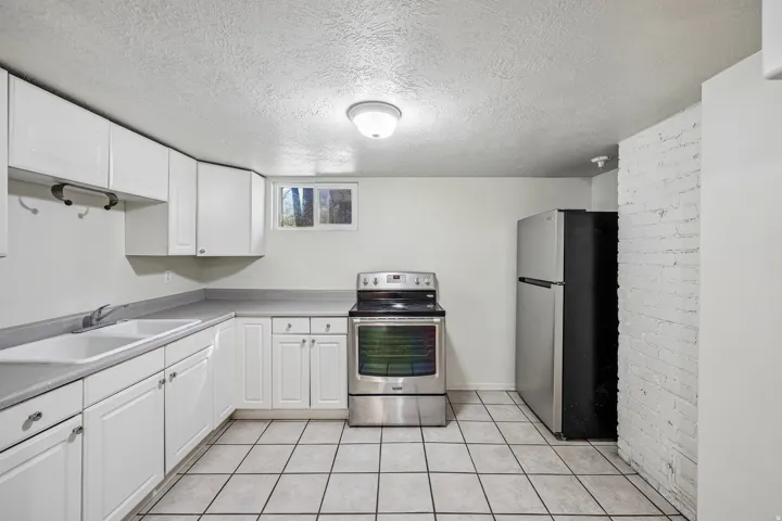 Galley-style kitchen featuring white cabinetry, stainless steel appliances including a gas range and refrigerator, ceramic tile flooring, and ample counter space for meal preparation