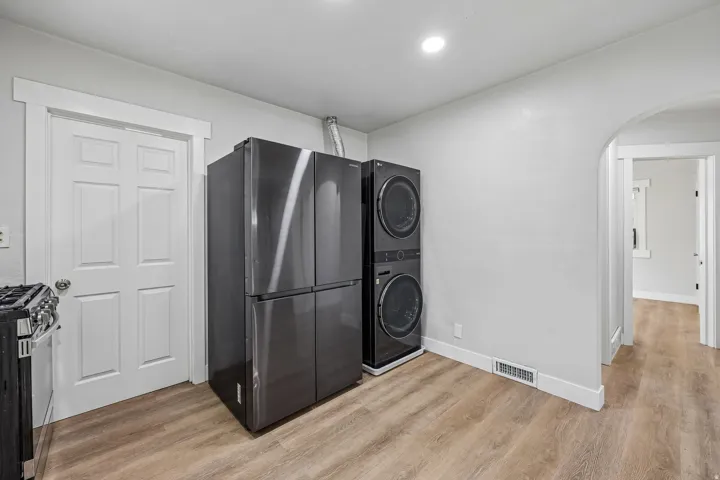 Laundry room featuring wood-finish flooring, recessed ceiling lighting, and stackable washer/dryer appliances